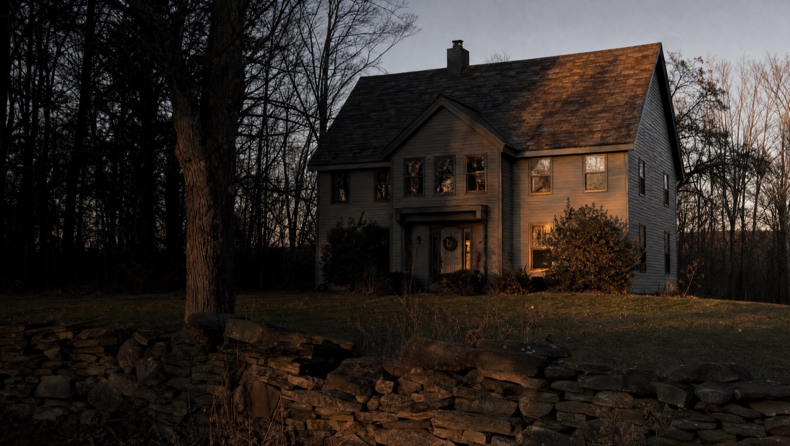 A two-storey home in Upstate New York at dusk, its roof, gables and lap siding running clean above a lit entry and mature planting.