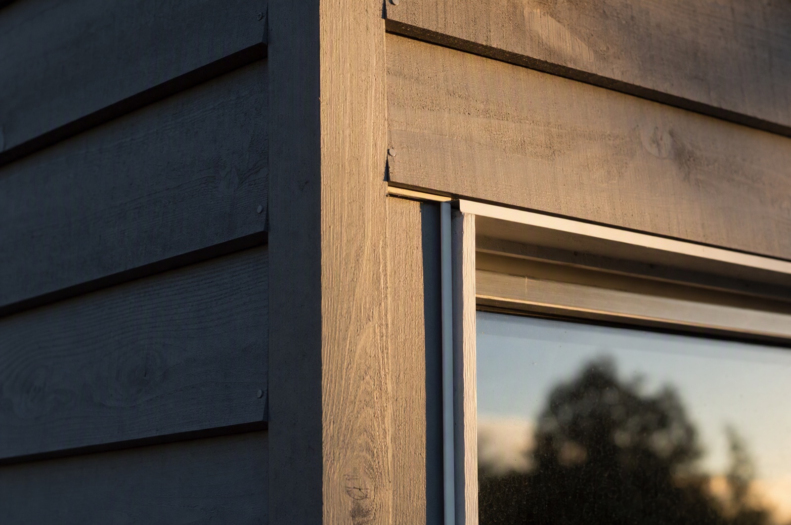 Finished siding detail where a wall meets a window: crisp white J-channel running the casing, a corner post catching the sun, lap courses stepping cleanly into it.