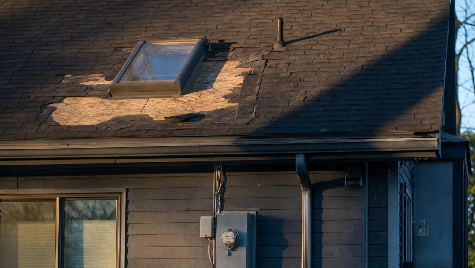 A localised failure around a skylight: shingles lifted and broken away, the sheathing beneath exposed, before targeted repair.