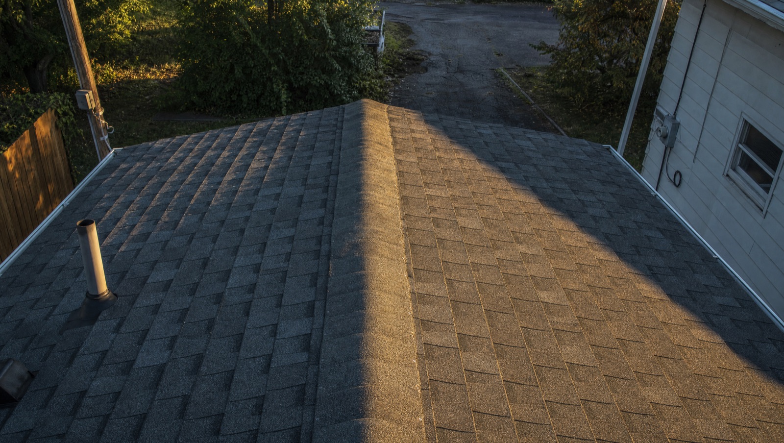 A completed Noble Edge roof: new architectural shingles running in clean courses up a hip to the ridge, the old farmhouse and driveway below.