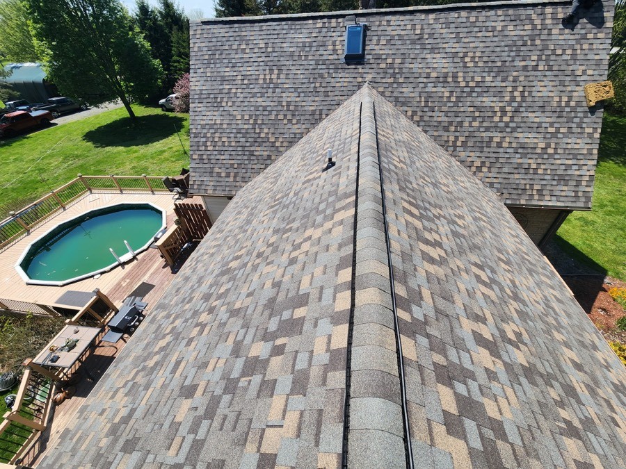 Aerial view of a completed multi-tone architectural shingle roof, ridge running to a hip, a pool and manicured backyard below.